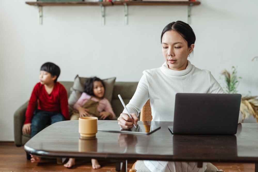 mum working on laptop at table with bored children behind